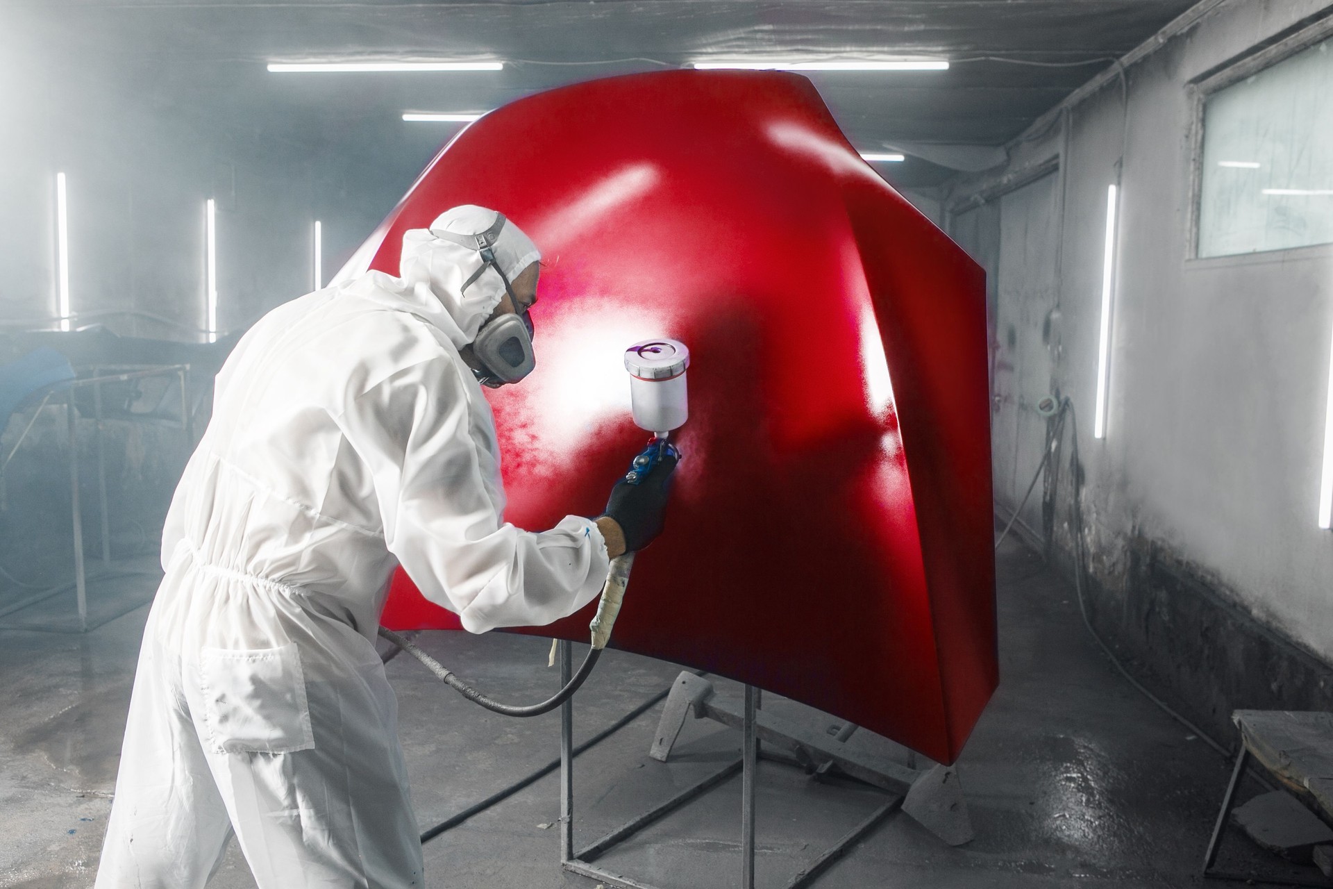 Car repairman artist hand wearing in protective workwear with airbrush spray painting the car body in the paint chamber.